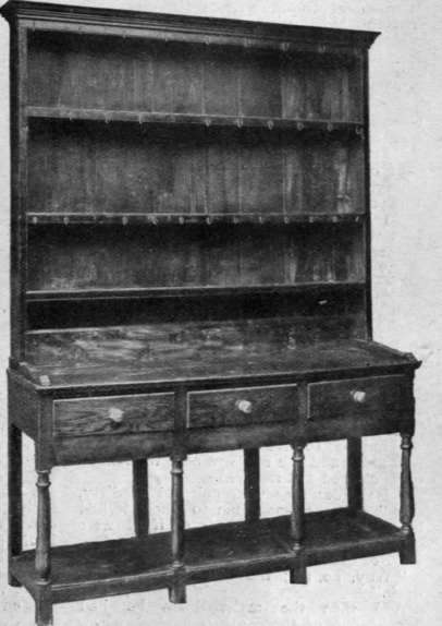 An English old oak dresser of simple but artistic design. In most specimens of genuine old oak the plate rack is of later date than the dresser itself
