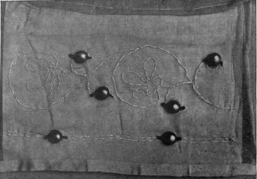 A grey silk net worked in white silk. Hollow gold cabochons held in place by tiny jet black beads are employed effectively