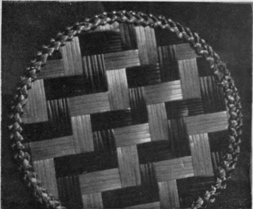 A small circular mat in coloured and natural straw, useful for placing under a hot dish or plate