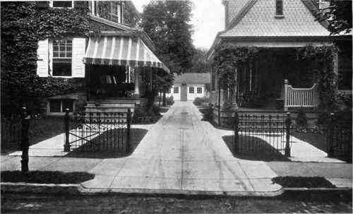 Fig. 31.   In this view is shown a simple, practical solution of a driveway in a contracted space. This is centered on the party line and the semi detached garages in the rear are easily accessible with ample turning space in front of them. An improvement here would have been to have two cement tracks, with grass between, rather than the entire driveway of cement. A little planting would relieve the harshness of the scene.   See pages 38, 39.