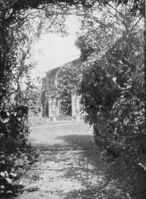 A creeper covered house seen through a pergola.