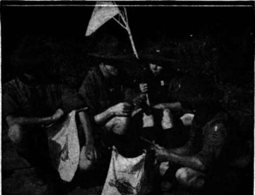 Gathering around their Scoutmaster to plan details of the evening camp fire
